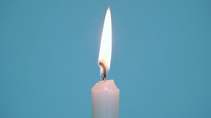 Close-up of a single wax candle burning. Isolated glowing candle on a blue background. Background...