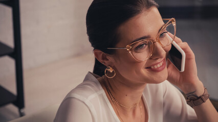 Cheerful designer in eyeglasses talking on mobile phone in atelier.