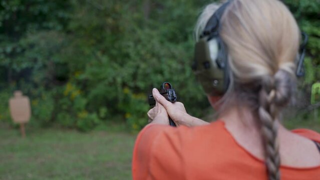 Closeup of mature, elderly woman fires a handgun at a shooting range target outside on a summer day.