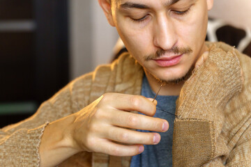 Mending clothes. A man is engaged in sewing. Household chores. Selective focus - obrazy, fototapety, plakaty