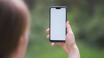 Female hand holding vertical black smartphone with green screen chroma key for tracking motion on the blurred city street background in sunny day.