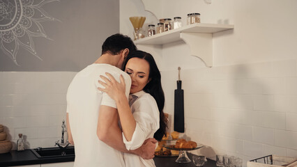 man hugging brunette and sensual woman in white shirt in kitchen.