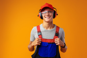 Young construction worker in helmet and uniform posing on yellow background in studio