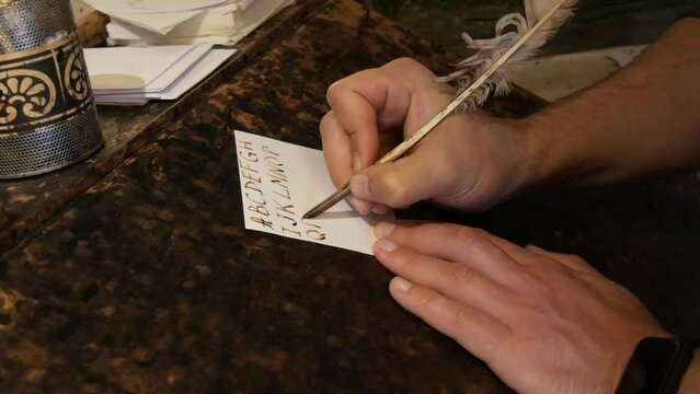 A man's hand writes the Latin alphabet in ink and bird pen feather. Installation under the old interior in the modern world