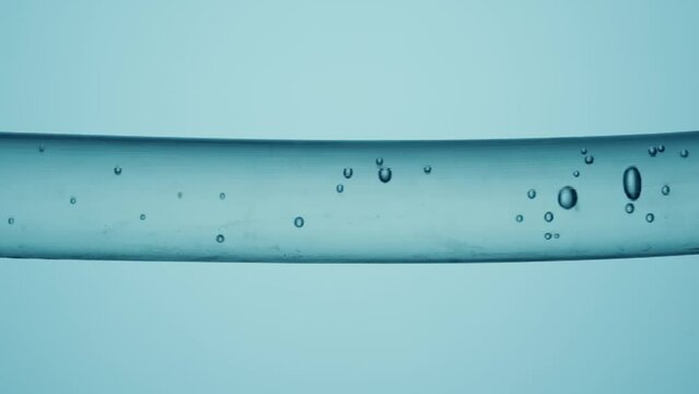 Macro shot of different sized clear bubbles flowing in glass tube with clear liquid on pale blue background. Vessel with clear liquid substance and moving bubbles.