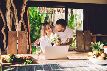 Pretty female graphic designer with modern laptop computer happy with received bouquet of...