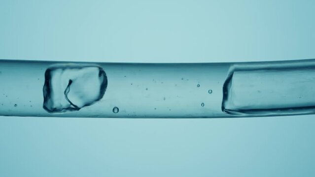 Transparent glass tube with flowing clear water and air bubbles on a blue background. Macro shot of the movement of a liquid substance with formation of bubbles.