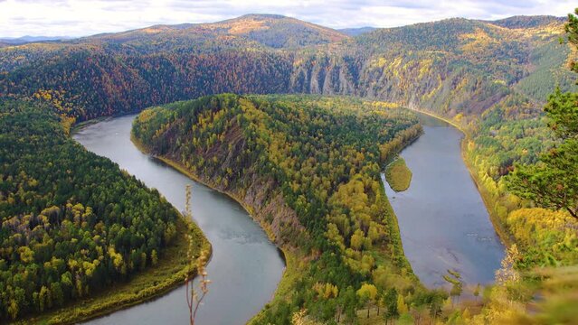 Windy autumn morning over the winding river. Moving clouds in the sky. Colorful autumn landscape with loop on meandering river among mountains in Siberia.