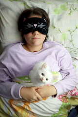 teen girl asleep with a sleep mask holding a white kitten