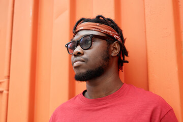 Single color portrait of young African American man against red wall in urban setting
