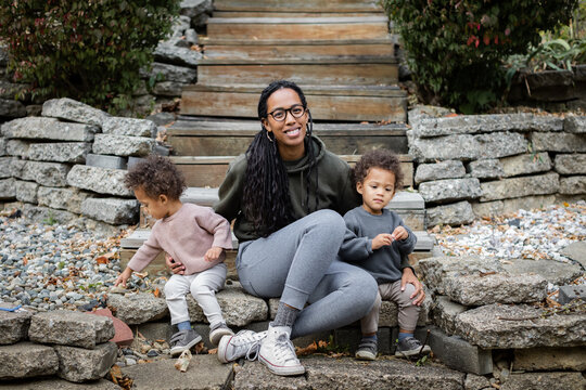 Black mom smiling with toddler twins on steps in backyard in fall 