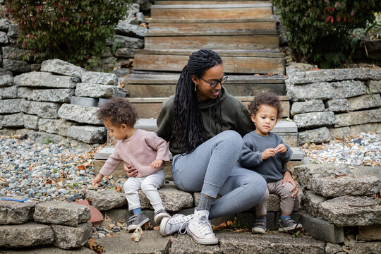 Black mom smiling with toddler twins on steps in backyard in fall  - Powered by Adobe