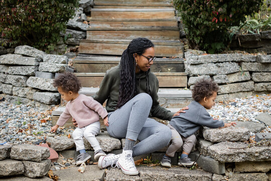 Black mom sitting with toddler twins on steps in backyard in fall 