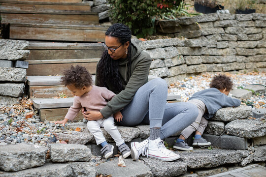 Black mom sitting with toddler twins on steps in backyard in fall 