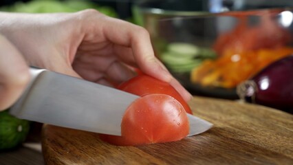 woman's hands using kitchen knife cutting fresh tomato on wooden cutting board. Healthy eating. Sliced tomato.