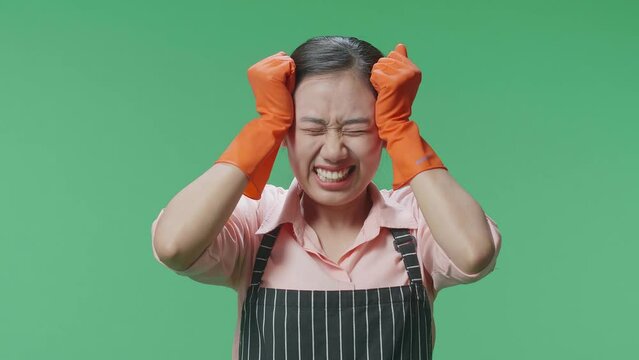 Close Up Of Asian Female Housekeeper With An Apron Have A Headache And Don'T Know Why While Standing In The Green Screen Studio
