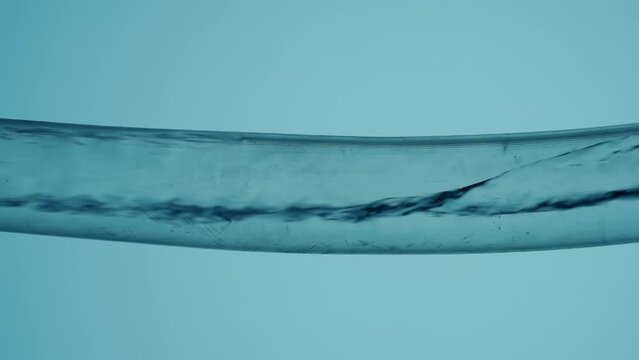 Water flowing in stream inside transparent glass tube on an isolated blue background. A clear liquid fills the tube forming small air bubbles. Laboratory research, chemical experiments.
