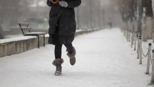 Slow motion of a woman's legs with furry boots and log winter jacket running in a park with heavy snow storm