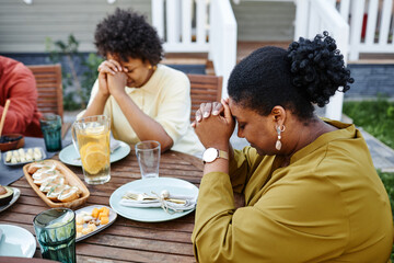 Fototapeta na wymiar Side view portrait of black young woman praying at table outdoors during family gathering