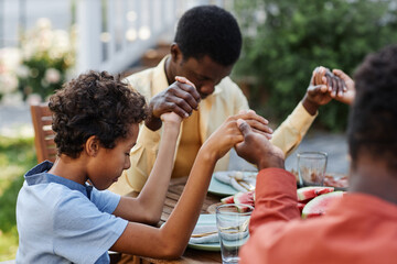 Portrait of young African American boy saying grace at table outdoors during family gathering and...