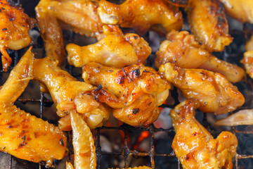 Close-up of chicken drumsticks and wings being grilled over charcoal.