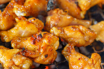 Close-up of chicken drumsticks and wings being grilled over charcoal.