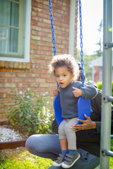 Black mother pushes biracial toddler on swing