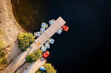 Pedal boats (pedalo, water-bicycle, pedalos) stay by wooden pier (marina) on the lake (Przylasek Rusiecki) bby drone (aerial view from above)