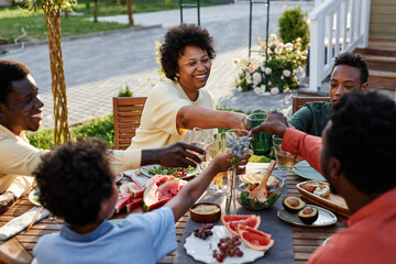 Portrait of smiling young woman clinking glasses with family and friends while enjoying dinner outdoors - Powered by Adobe