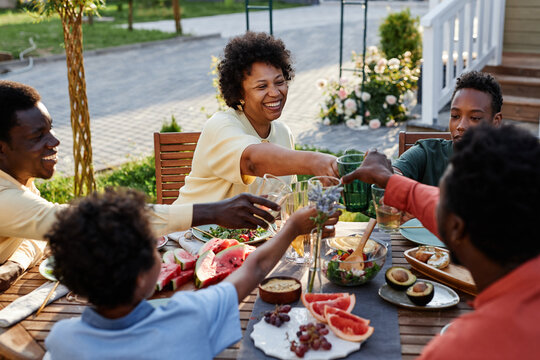 Portrait of smiling young woman clinking glasses with family and friends while enjoying dinner outdoors
