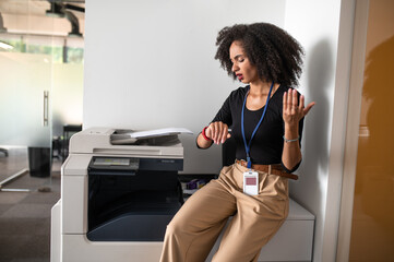 Young woman sitting near xerox and looking at her watch