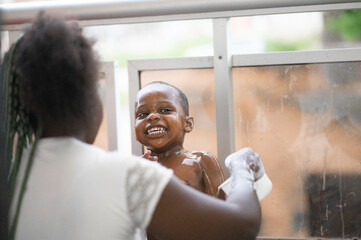 La giovane madre africana che lava il suo figlio in un secchio d'acqua 