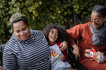 Black son with aunt and mother laughing on bench in park