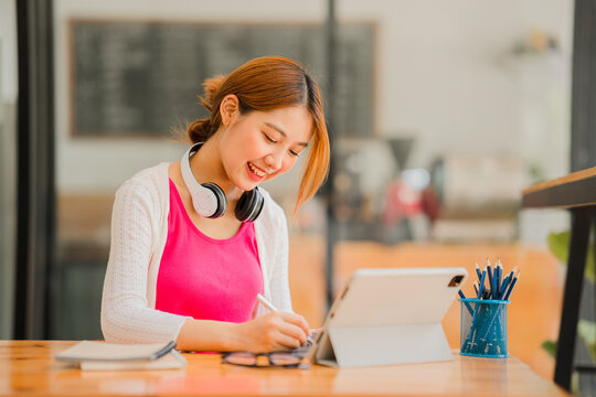 Asian female students studying online e-learning with tablet sitting at a desk and holding a pen distance learning concept at coffee shop