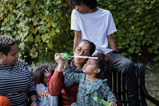 African American family relaxing on bench in park in fall and blowing bubbles