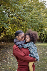 Black mother holds and carries daughter while looking at her in park
