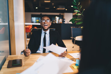 Cheerful black businessman sitting at table with documents in office