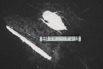 Cocaine with rolled dollar on black table. A rolled up dollar bill for drug use. Drug epidemic...
