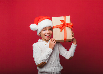 Cute little boy in a Santa Claus hat holding a gift box on a red background. a child with a New Year's gift for Christmas. new year