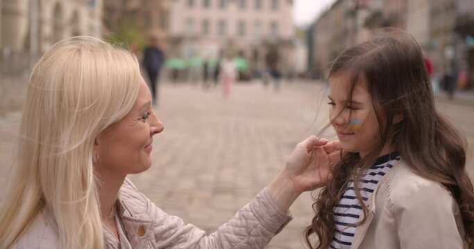 Mother hugging her daughter with Ukrainian flag on a cheek