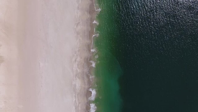 Drone view of beautiful seamless never ending footage while turquiose sea waves breaking on sandy coastline. Aerial shot of golden beach meeting deep blue ocean water and foamy waves.