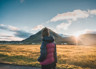 Woman in winter jacket walking through Stapafell mountain and sunlight shining in the sunset at Arnarstapi village