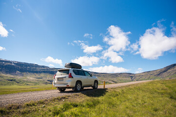 Fototapeta premium Large car parked on dirt road among the mountain and meadow on sunny day in summer