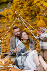 Happy family on a beautiful fall picnic in the park. Cozy autumn vibes. Young father, mother and their cute son spending quality time together, having fun. in the park