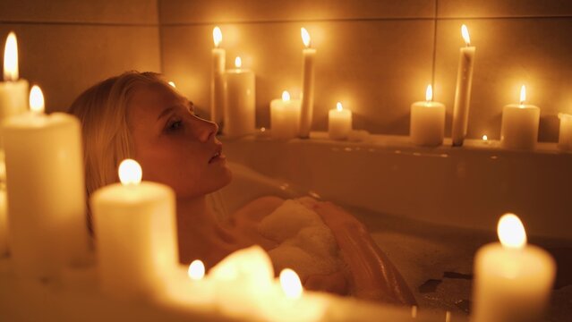 Relaxed woman washing hands in bath in slow motion. Top view of pretty lady enjoying in luxury bathroom with candles.