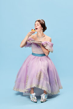 Beautiful charming girl in lilac color medieval dress as young queen or princess on blue background. Eras comparison, beauty, art, emotions and vintage fashion style