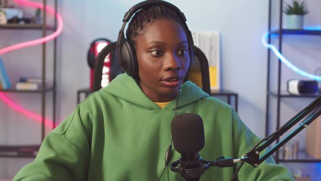 Chest up of young Black woman in headphones talking to other players via mic while playing online multiplayer game on computer at home