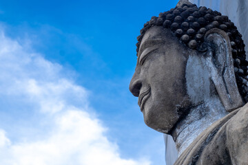 detail of the face of a representation of the buddha with his eyes closed, on blue nature sky background, the from under view