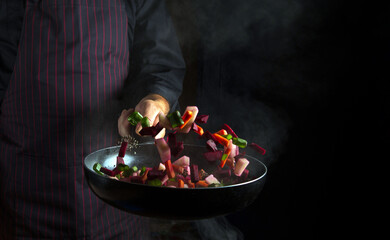 Cooking vegetables in a frying pan by the hands of a chef. Food concept on black background. Vegetable menu or recipe for hotel