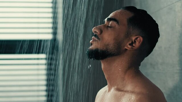 Side view Hispanic Latino Indian handsome bearded naked man guy washes in shower bath rain hot water washing male face hair refreshed after workout in gym morning hygiene procedure refreshment clean